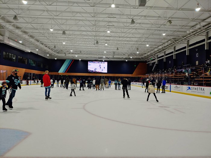 People skating on ice rink with big screen TV in the background showing hockey game